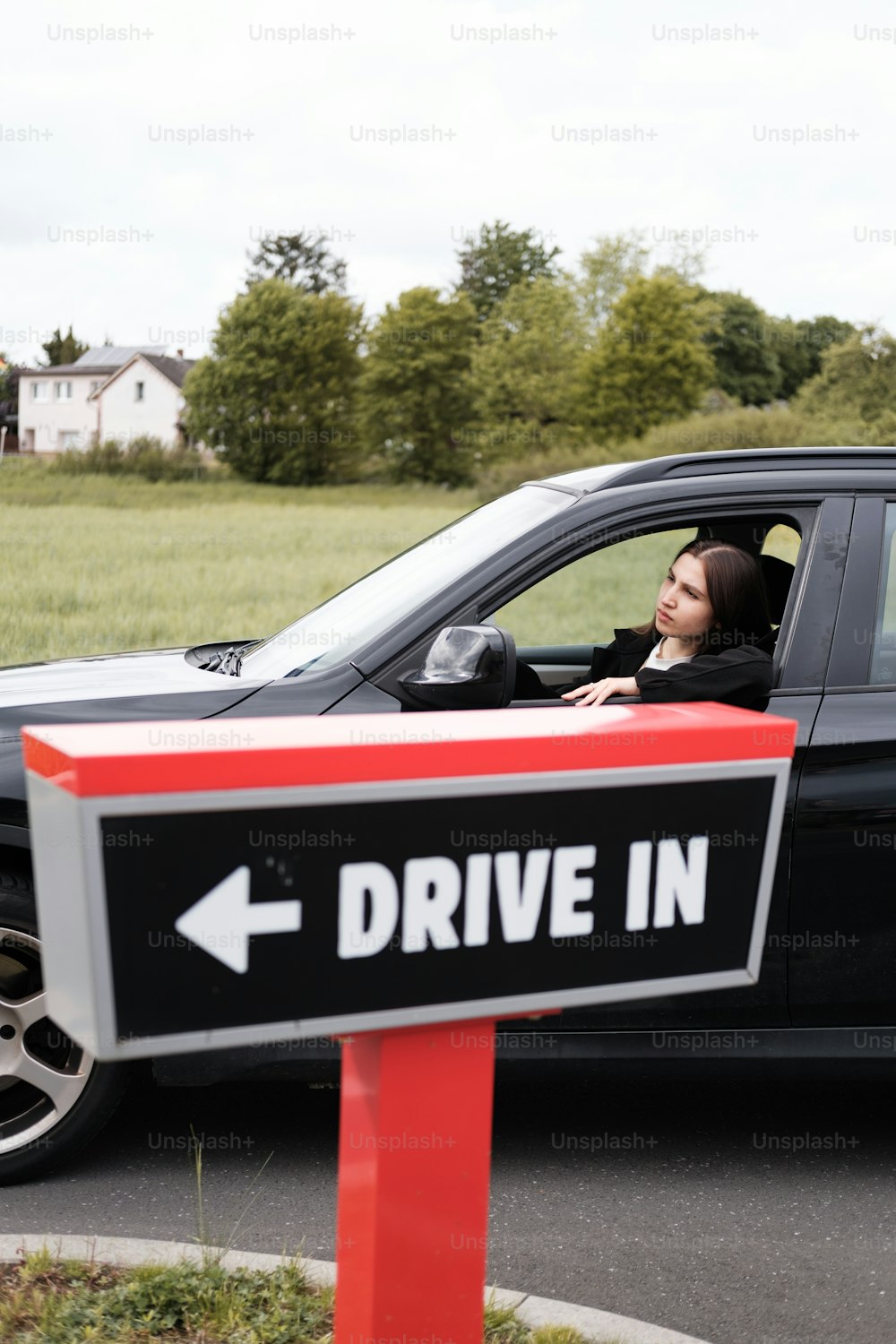 Una mujer sentada en un automóvil con un letrero de drive in frente a ella