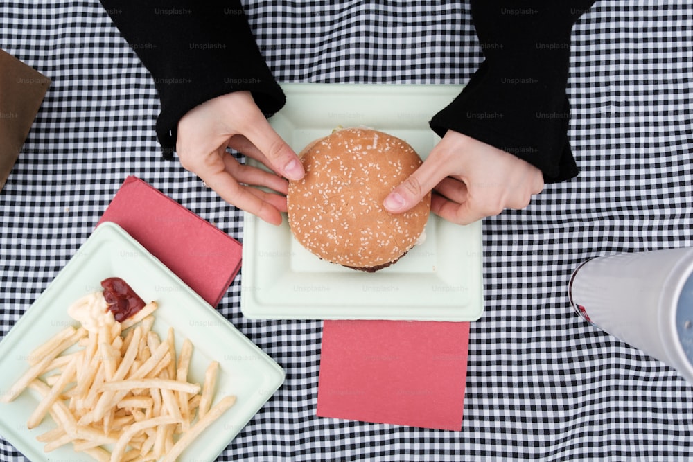 a person holding a hamburger over a plate of fries