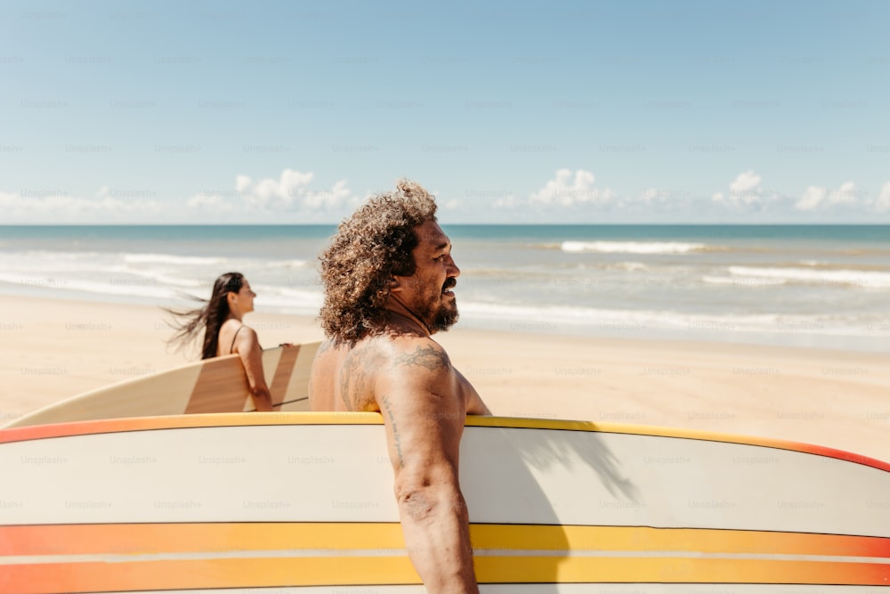 a man holding a surfboard next to a woman on the beach