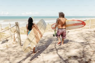 a man and a woman walking on the beach with surfboards