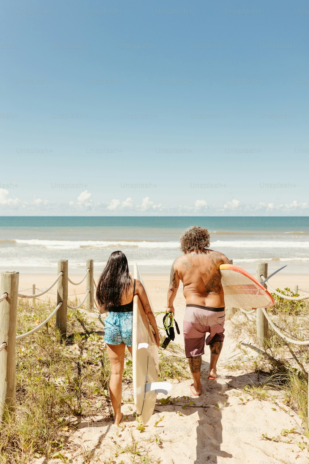 a man and a woman walking on the beach with surfboards