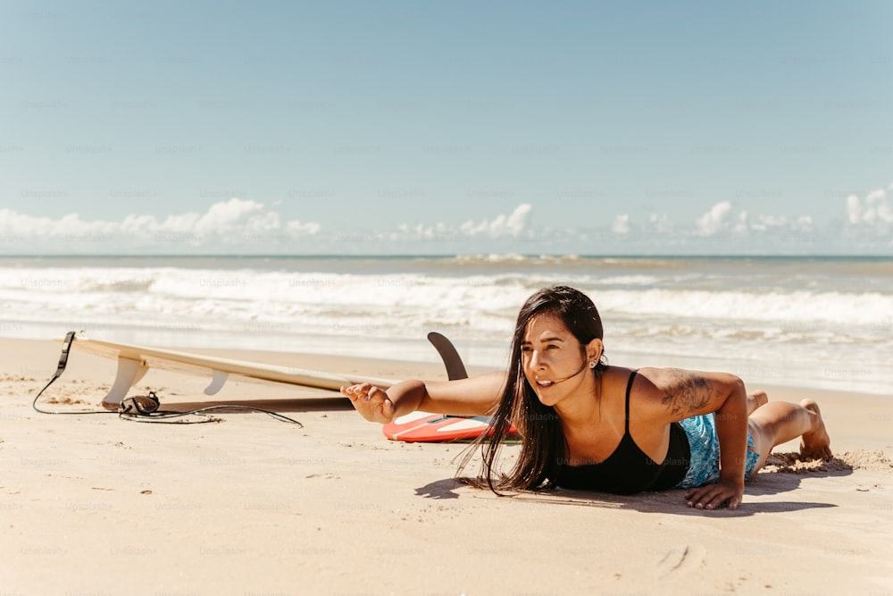 a woman laying on the beach next to a surfboard