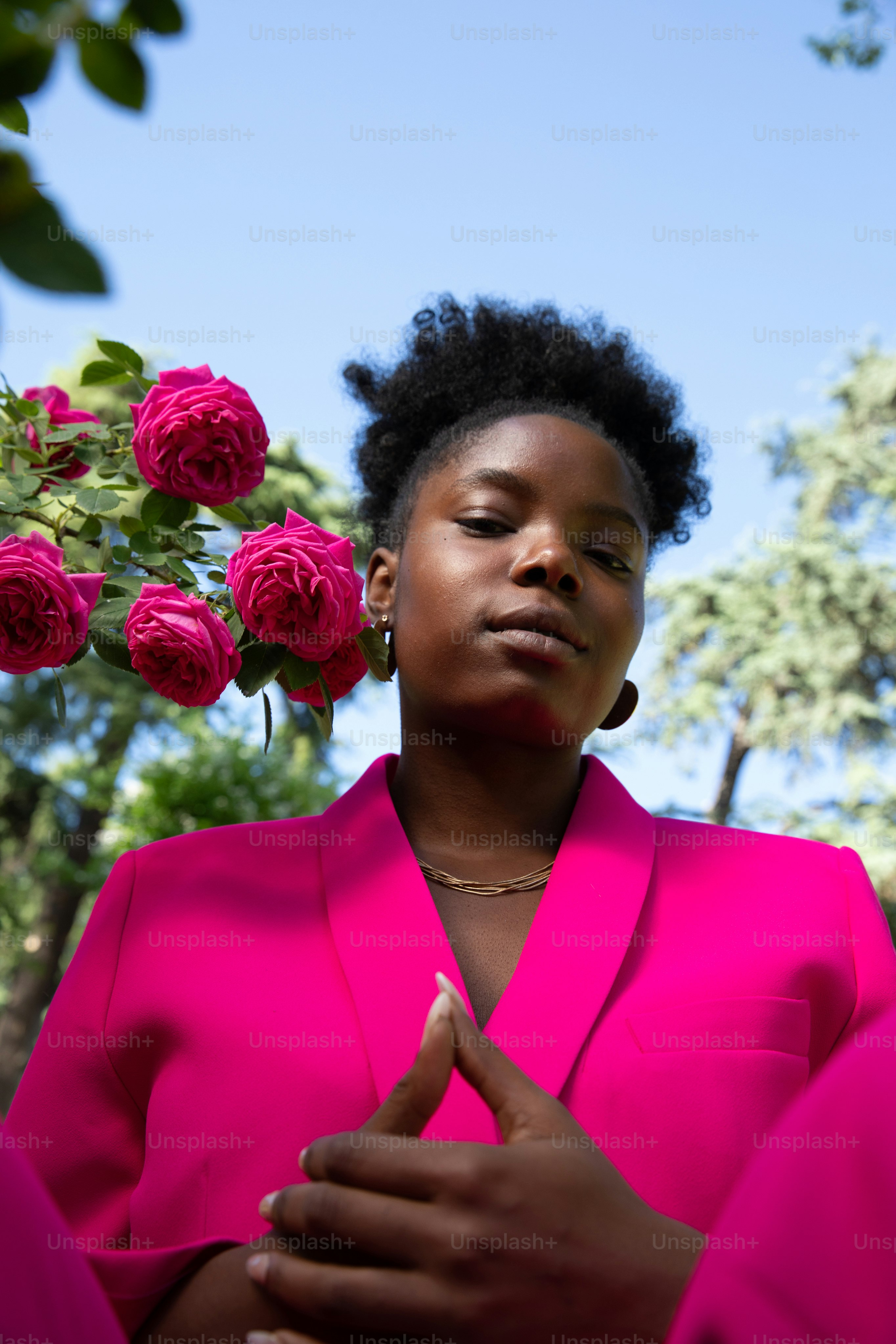 バラの前に立つ明るいピンクのシャツを着た女性
