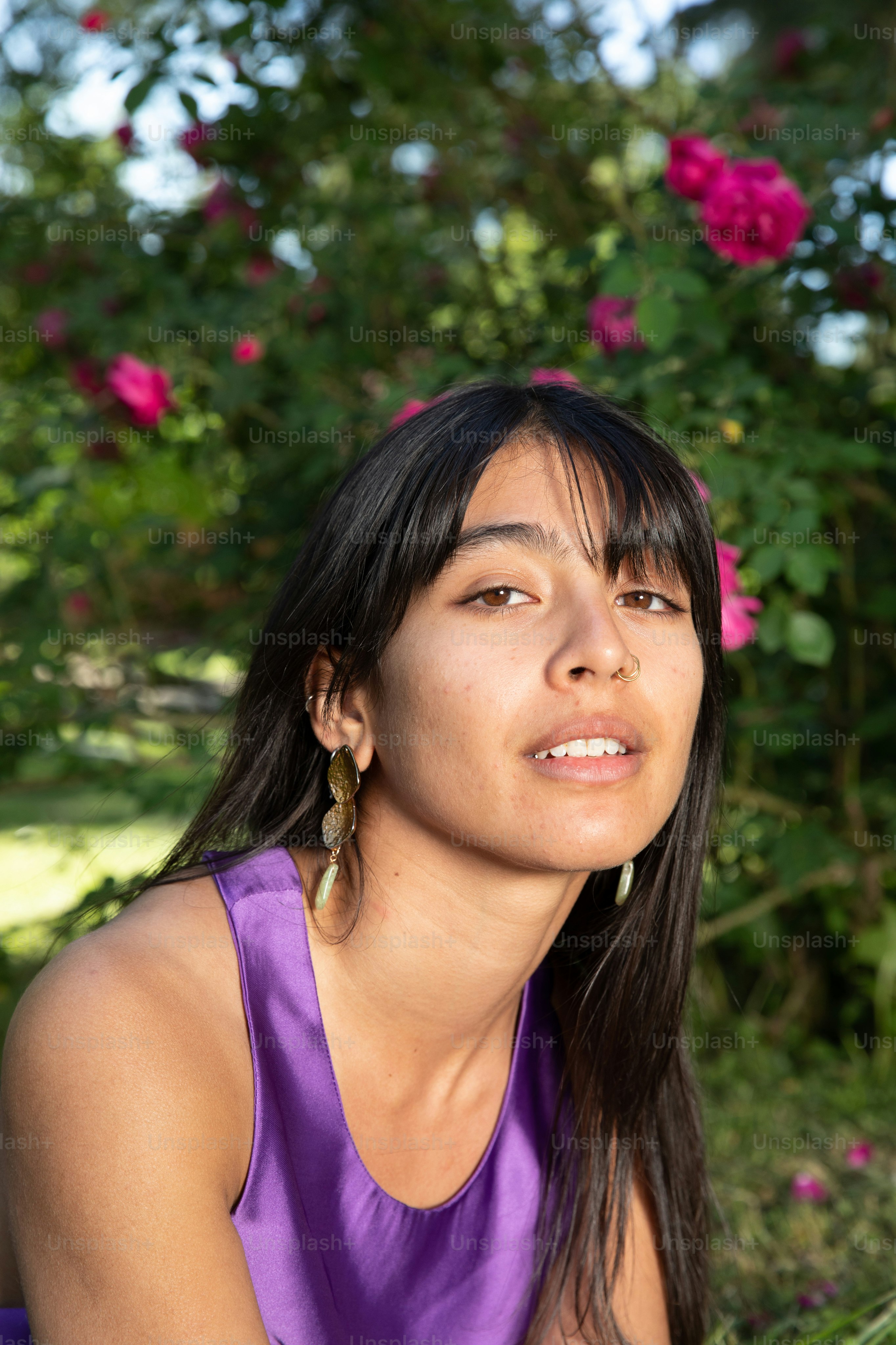 uma mulher em um top roxo sentada em frente a um arbusto