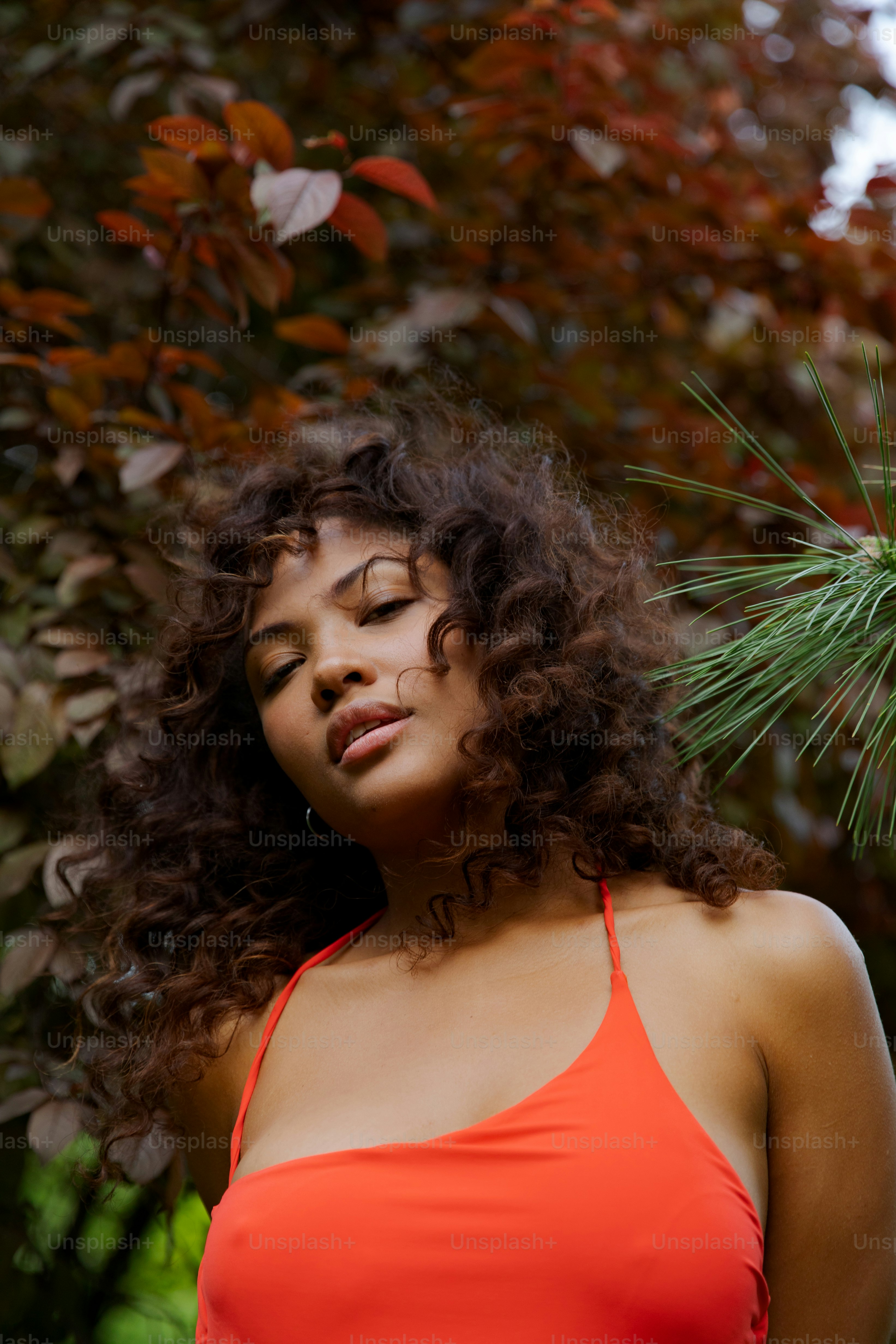 uma mulher em um top vermelho em pé na frente de uma árvore