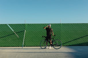 a man standing next to a bike next to a green fence