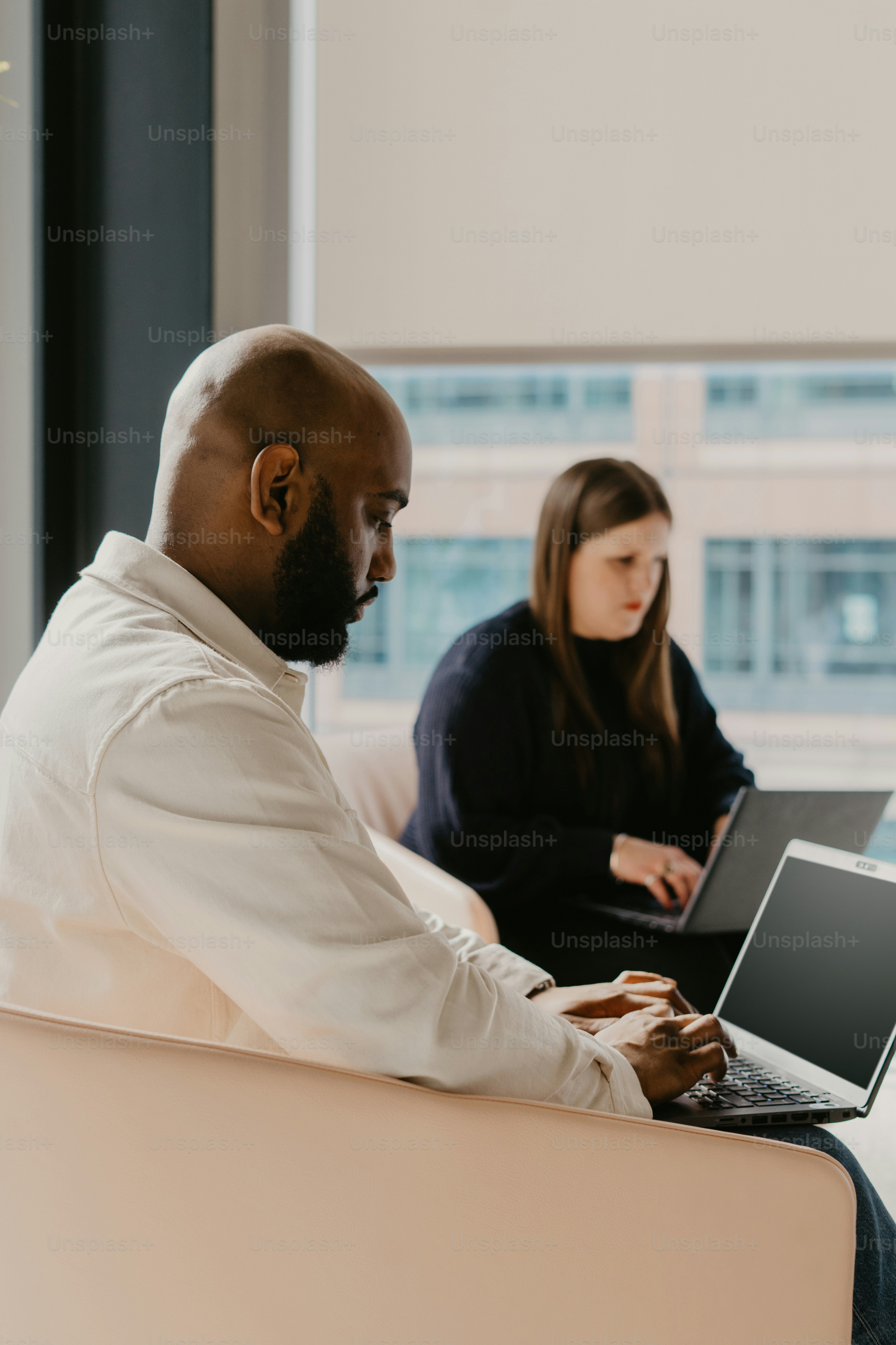 Un hombre y una mujer sentados en un sofá usando computadoras portátiles