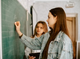 duas meninas escrevendo em um quadro negro em uma sala de aula