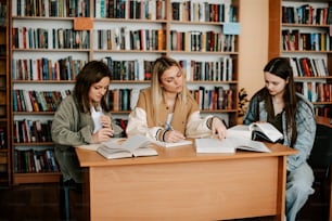 three girls sitting at a table in front of a bookshelf
