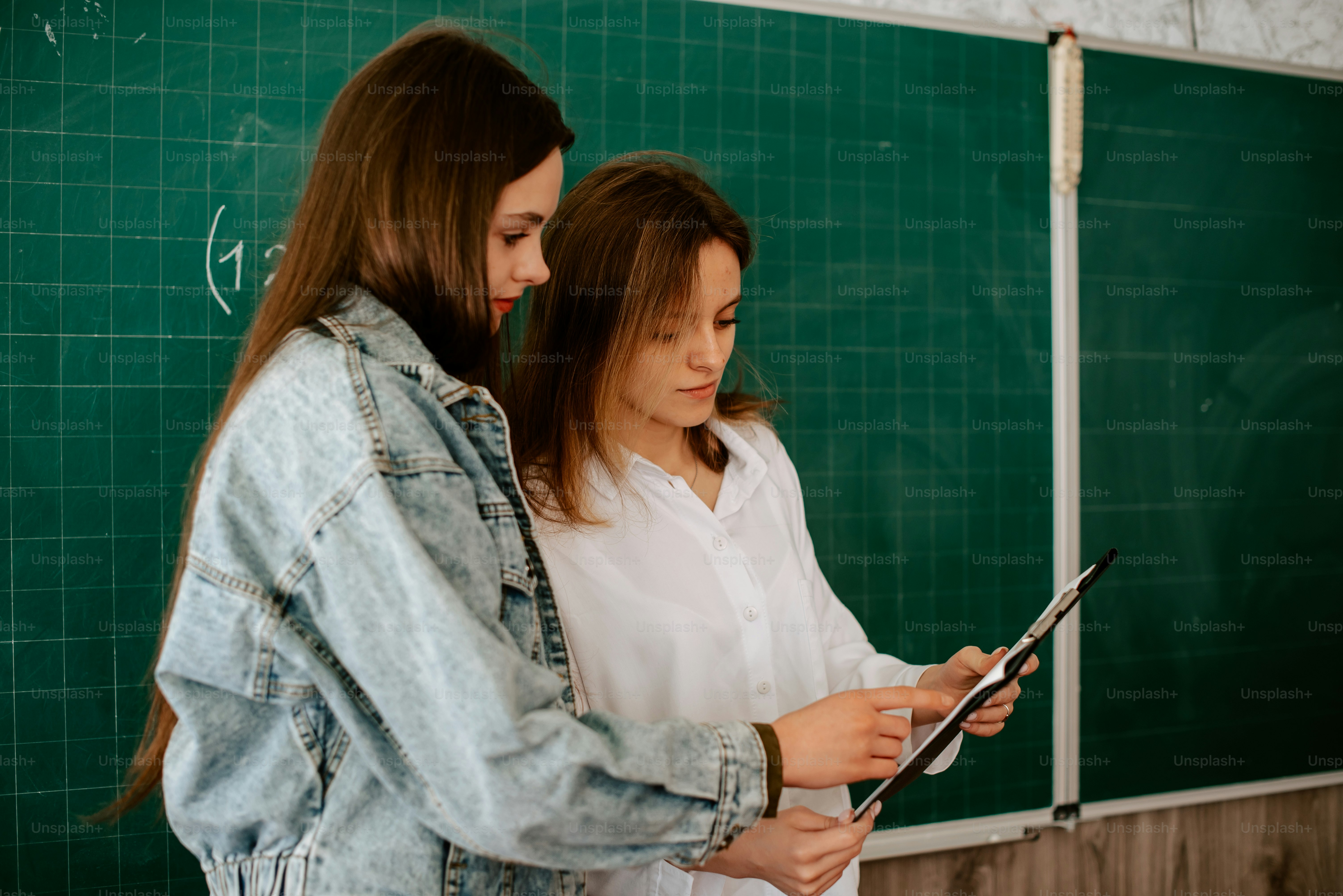 黒板の前に立つ2人の女の子がタブレットを見ている