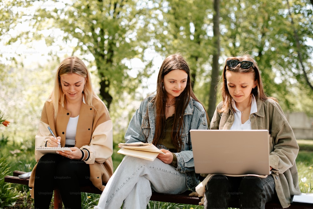 three girls are sitting on a bench and looking at a laptop