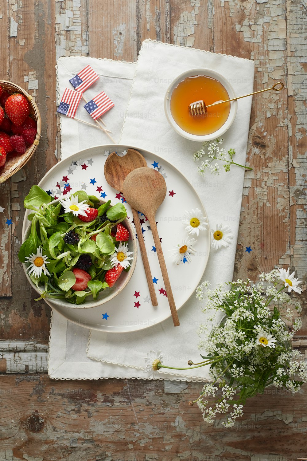 a white plate topped with a salad next to a bowl of strawberries