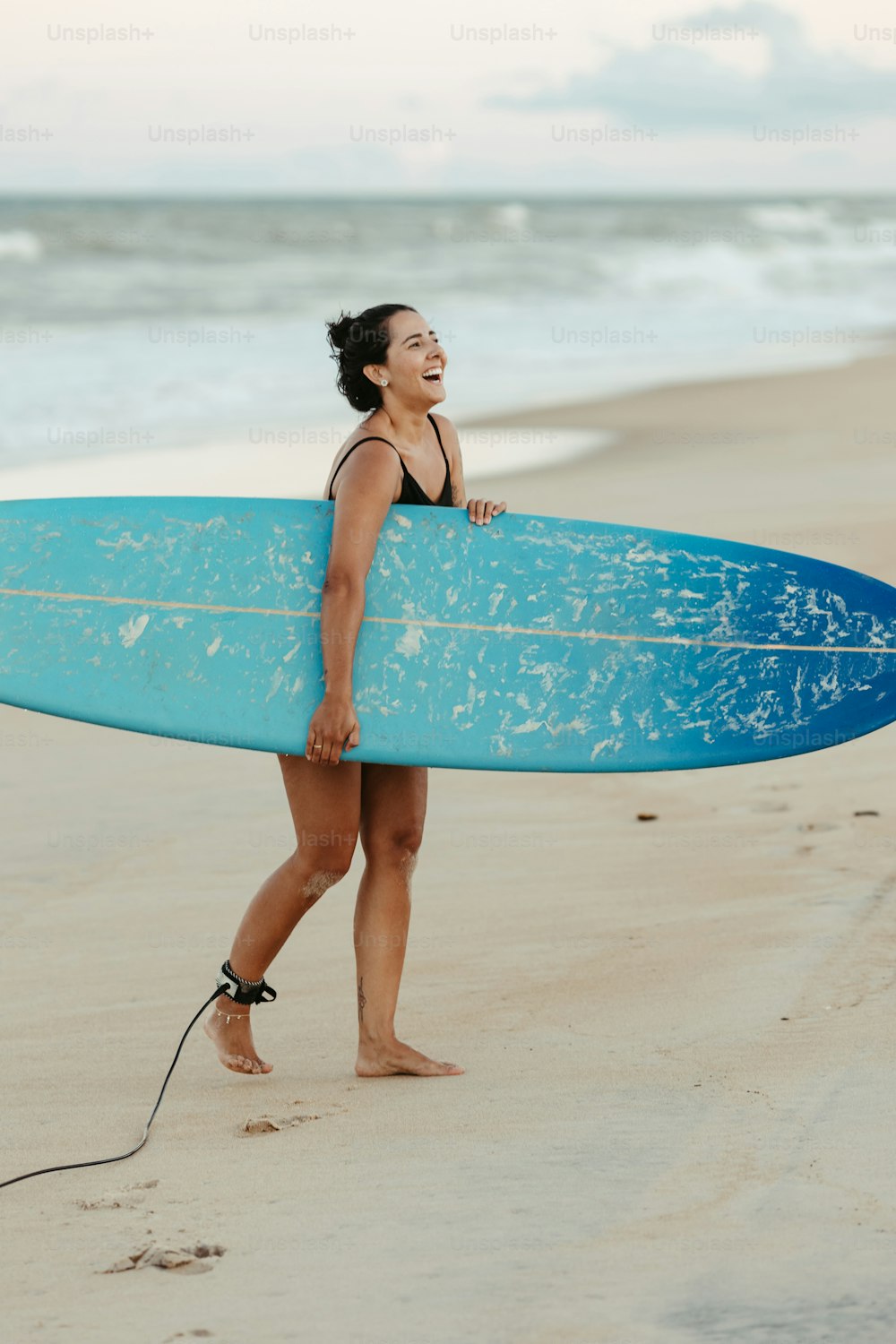 uma mulher andando na praia com uma prancha de surf