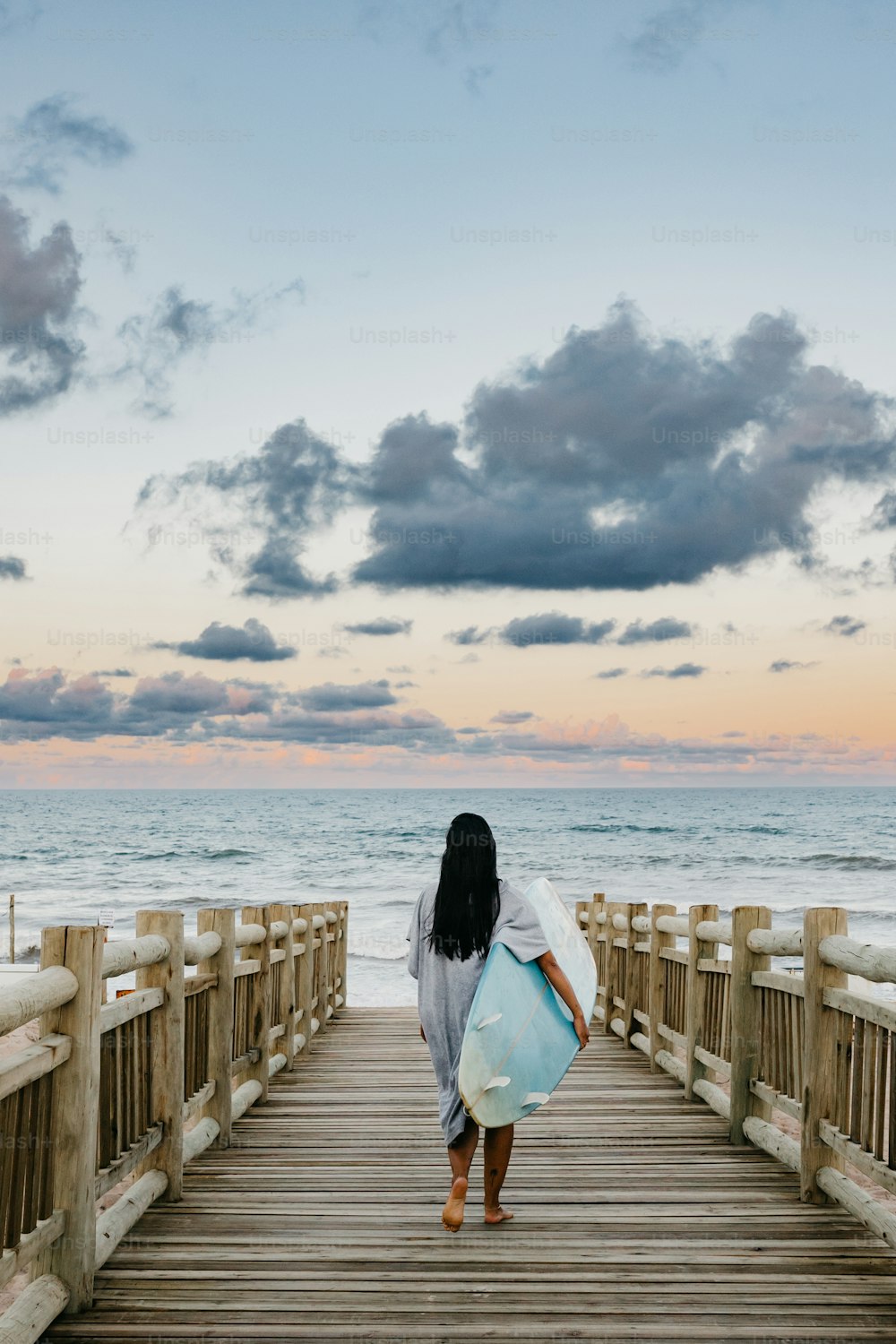 a woman carrying a surfboard walking down a pier