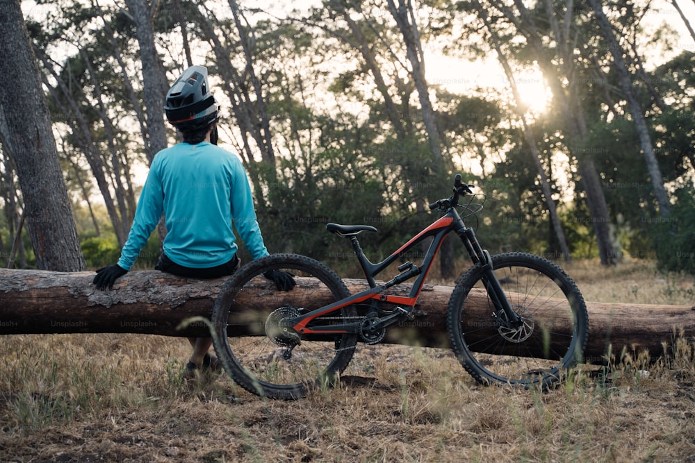 uma pessoa sentada em um tronco com uma bicicleta