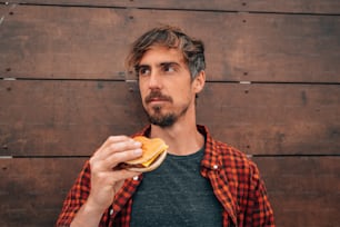Un uomo che tiene un panino davanti a un muro di legno
