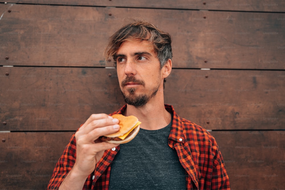 a man holding a sandwich in front of a wooden wall