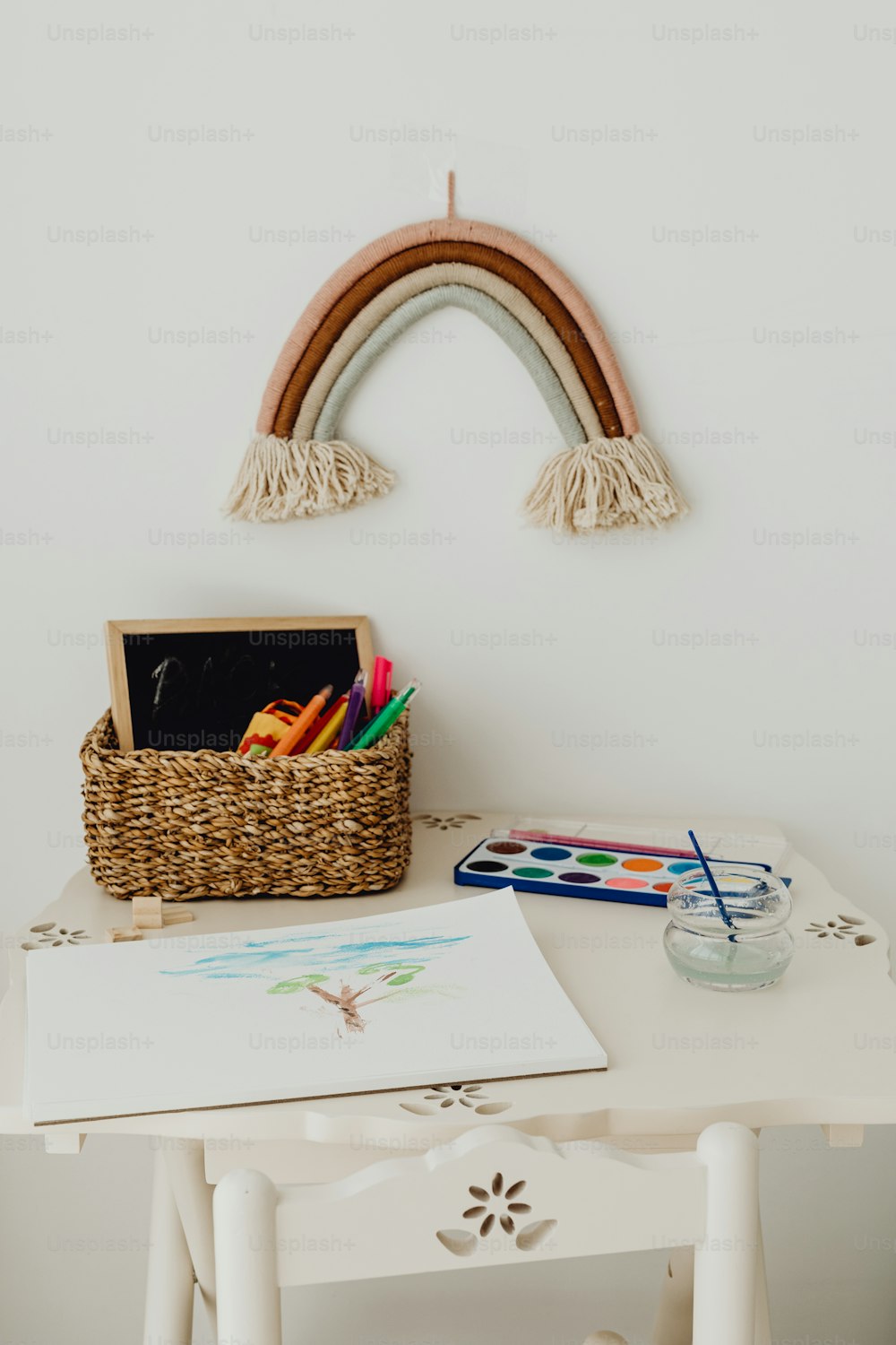 uma mesa branca com uma cesta de lápis de cor e um arco-íris na parede