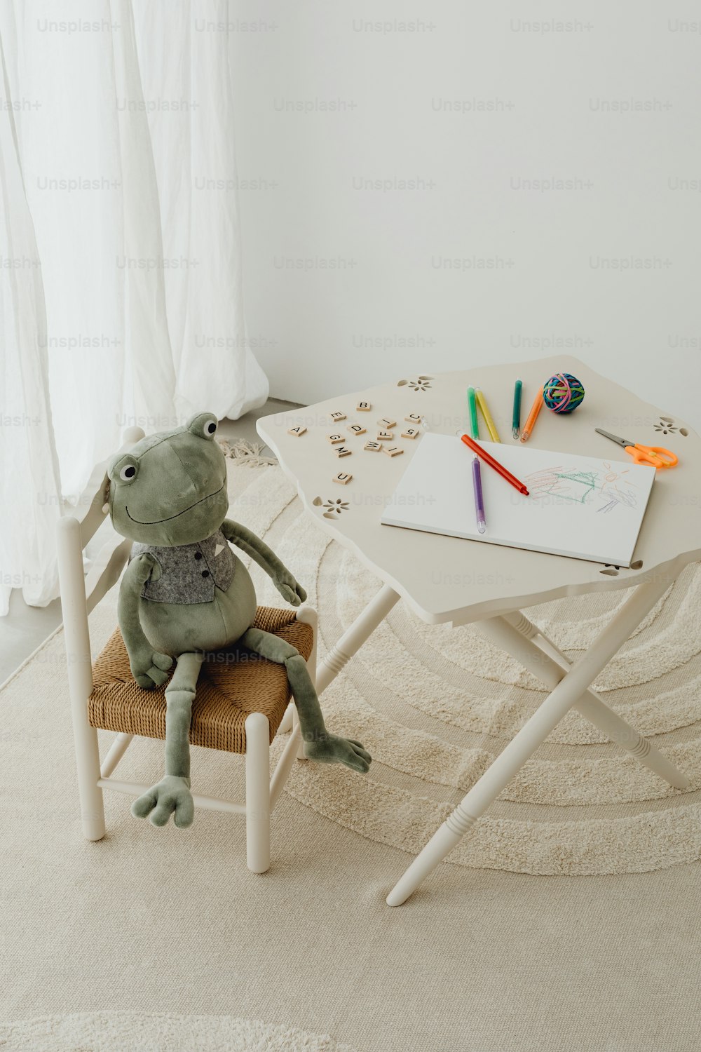 a stuffed frog sitting on a chair in front of a table