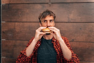 a man eating a hamburger in front of a wooden wall