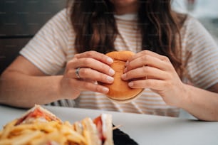 uma mulher sentada em uma mesa com um hambúrguer nas mãos