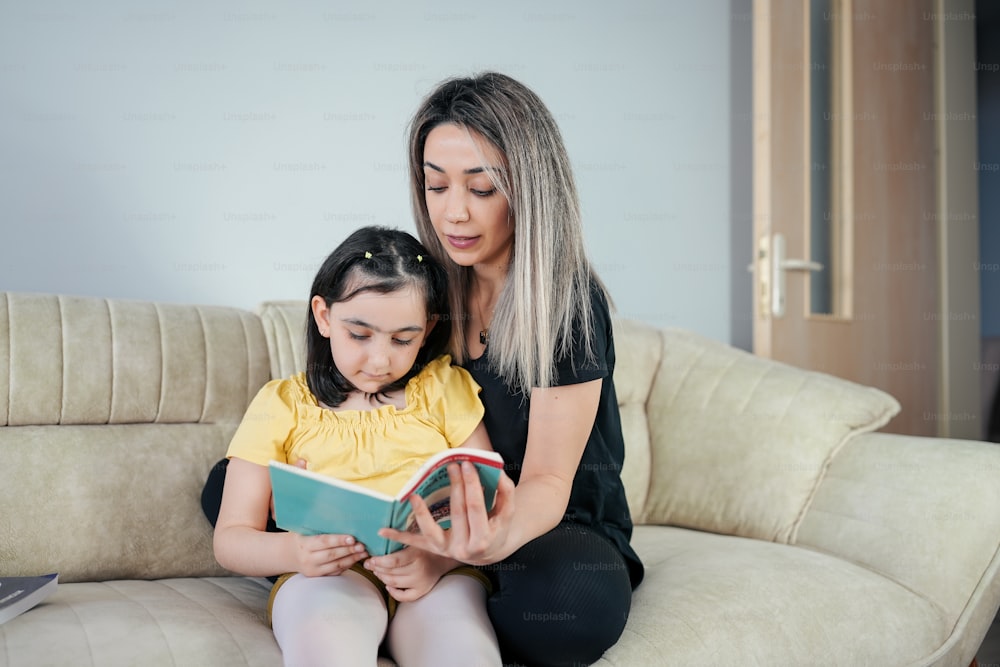 a woman sitting on a couch reading a book to a little girl
