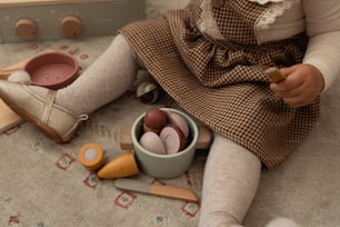 a little girl sitting on the floor next to a bowl of eggs