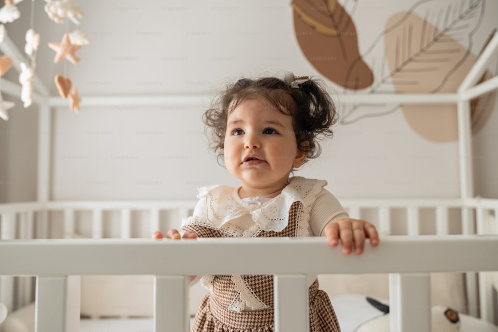 a little girl standing in her crib looking at the camera