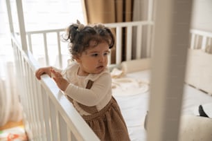 a little girl standing in a crib looking at the camera