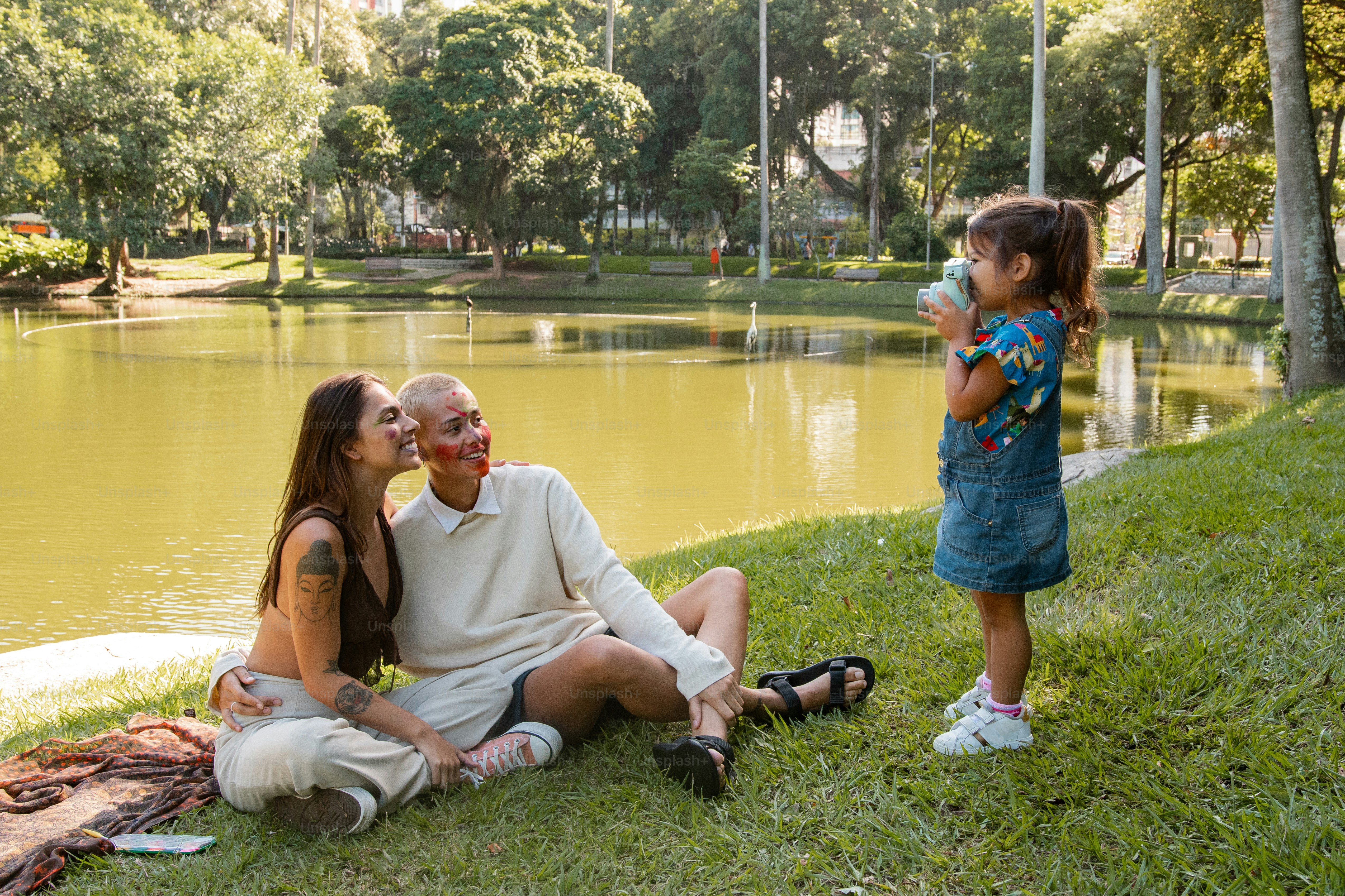 a woman and a child sitting on the grass near a pond