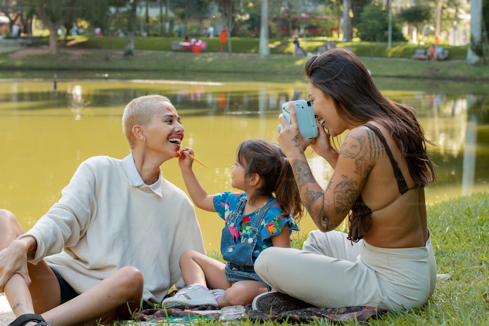 a woman and two children sitting on the grass near a pond