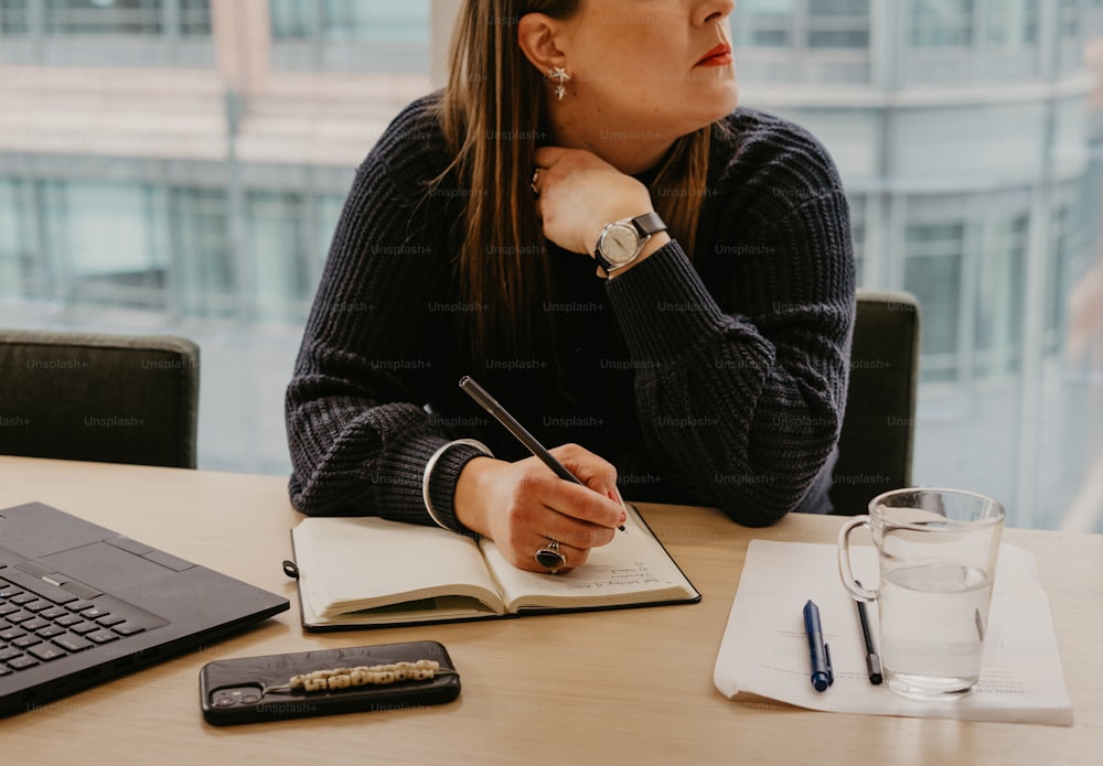 a woman sitting at a table with a notebook and pen