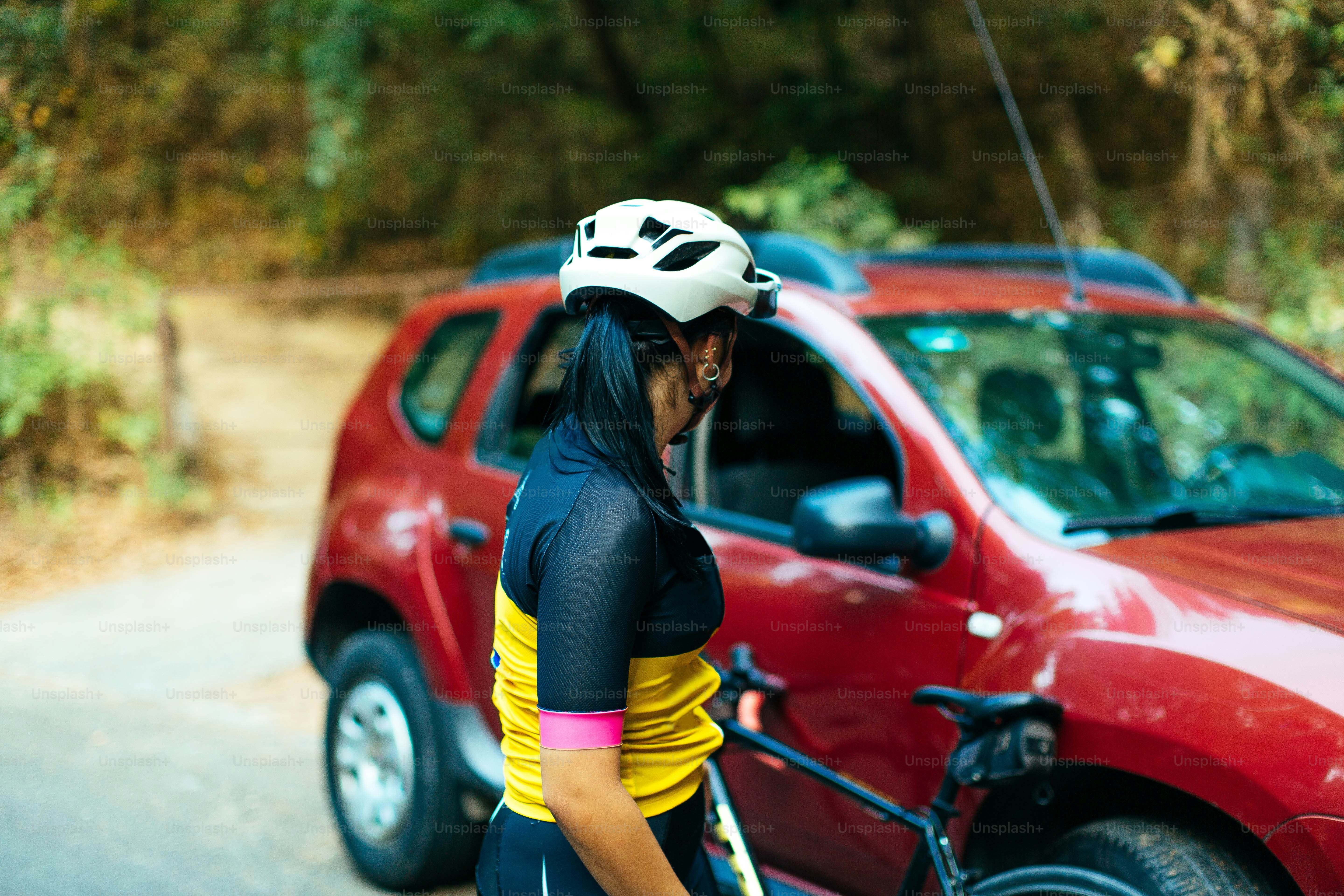 a woman with a helmet on standing next to a red car