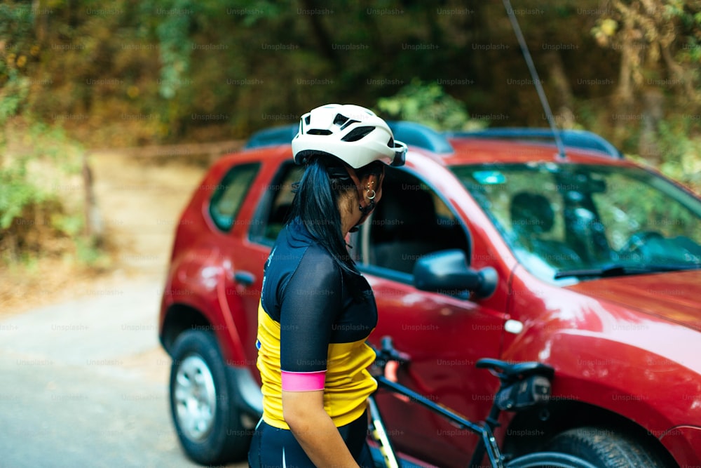a woman with a helmet on standing next to a red car
