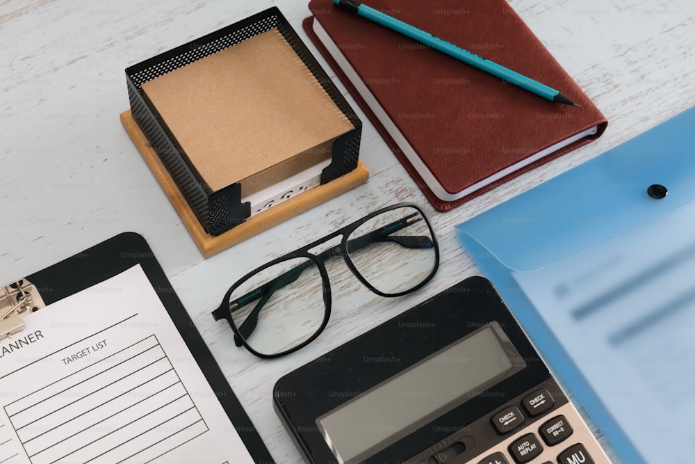 a desk with a calculator, pen, glasses, and a clipboard