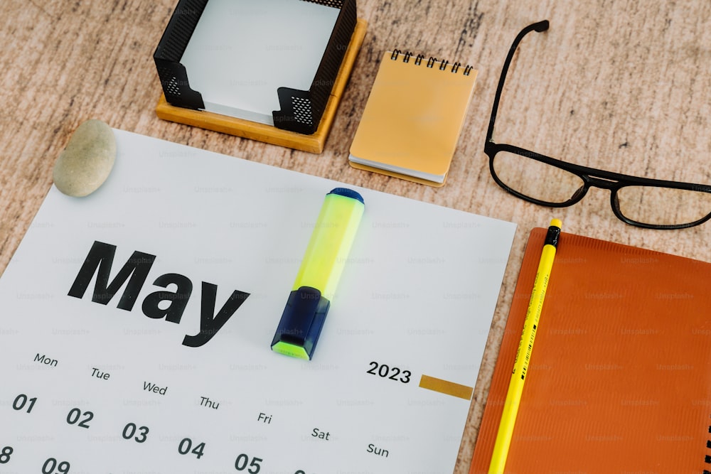 un escritorio con un calendario, bolígrafo, anteojos y un bloc de notas