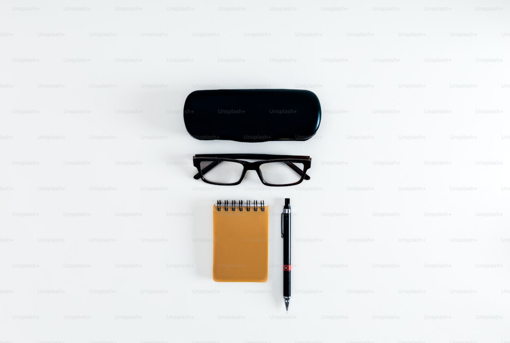 un par de gafas, bolígrafo y cuaderno sobre una superficie blanca