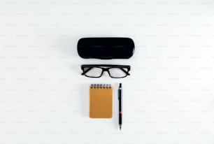 a pair of glasses, pen and notebook on a white surface