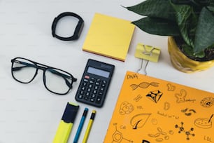 ein Schreibtisch mit Taschenrechner, Notizbuch, Stift, Brille und einem
