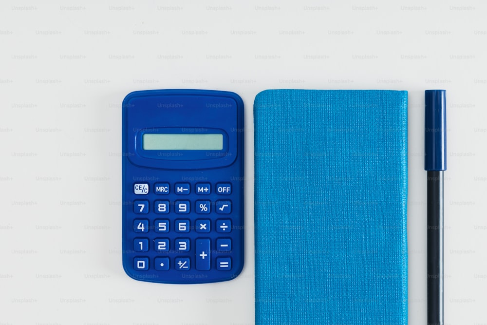 ein blauer Taschenrechner neben einem Notizbuch und einem Stift