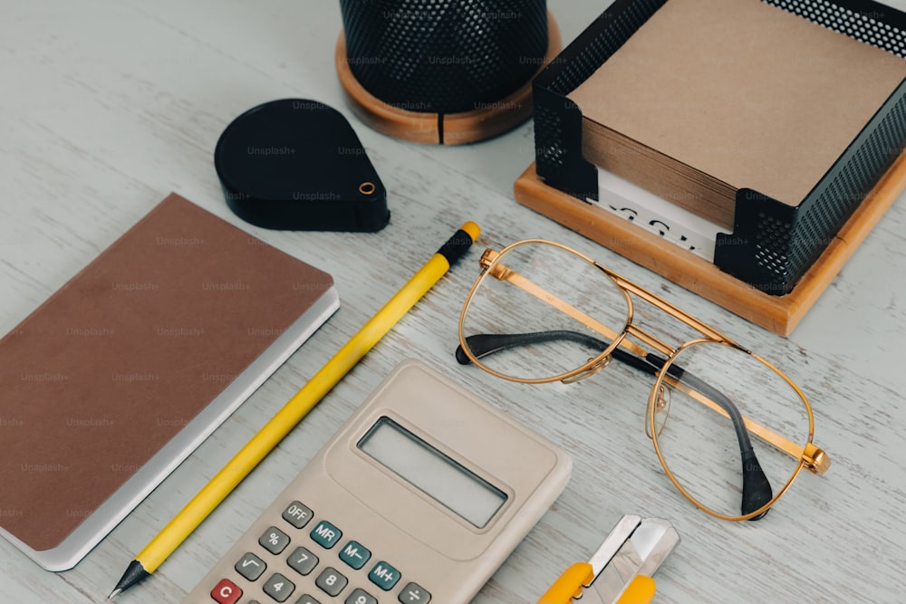 uma mesa com calculadora, caneta, óculos e caderno