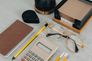 a desk with a calculator, pen, glasses, and a notebook