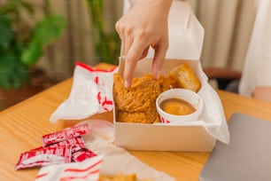 a person reaching for a piece of fried chicken in a box