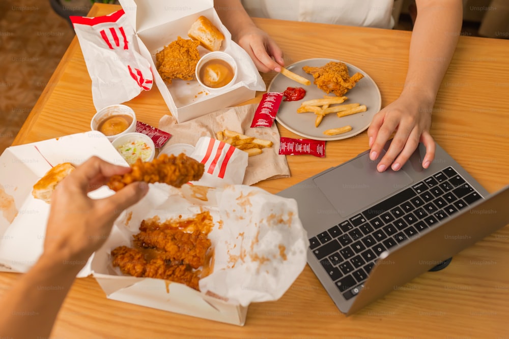 una persona seduta a un tavolo con del cibo e un computer portatile