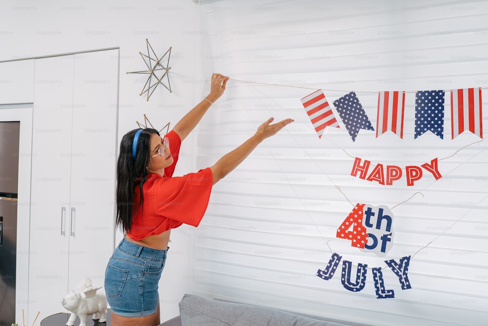 a woman in a red shirt and blue shorts holding up a fourth of july banner