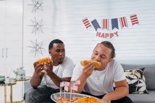 two people sitting on a couch eating hot dogs