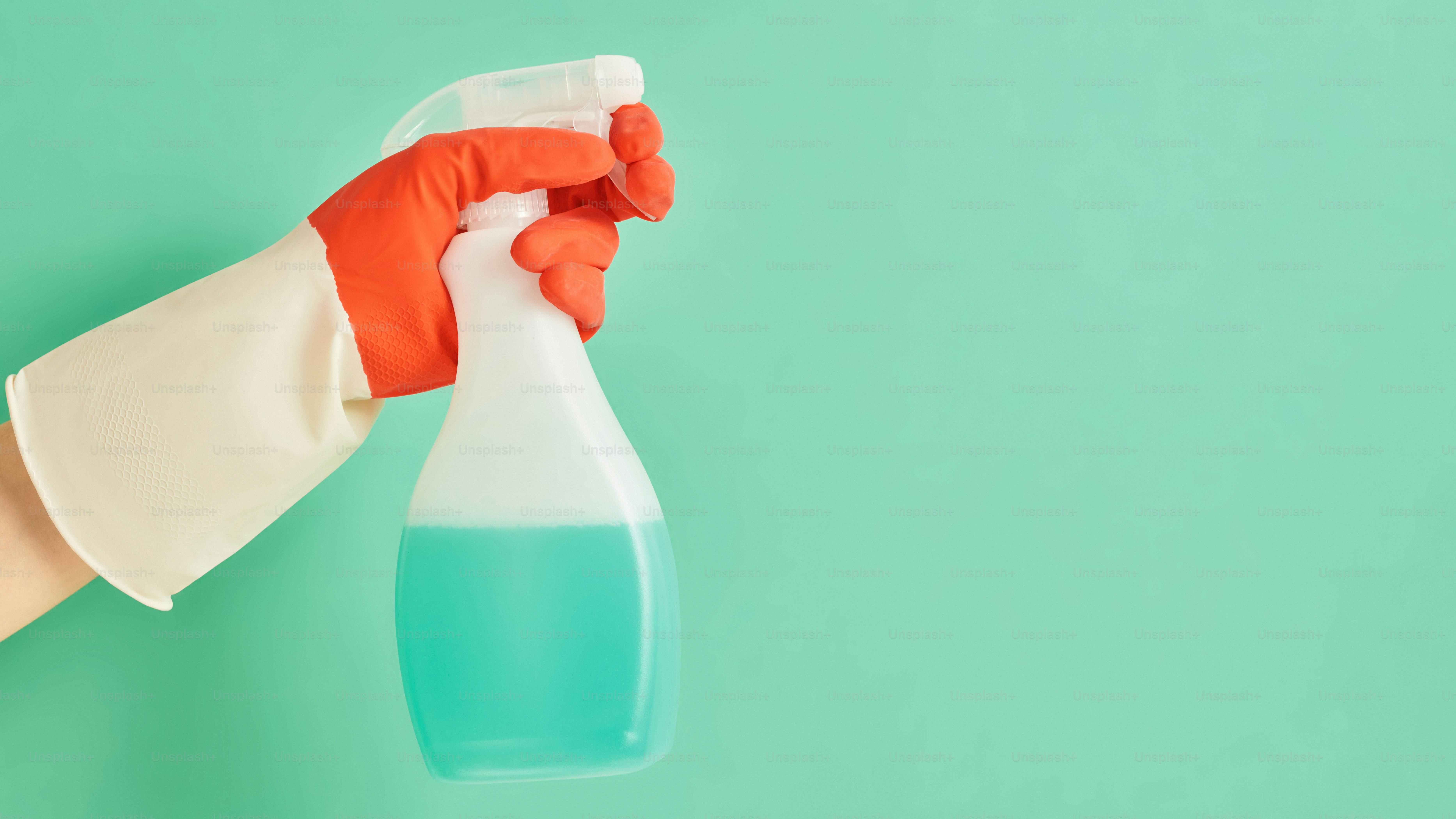 A hand in a rubber glove holding a cleaner on a colored background