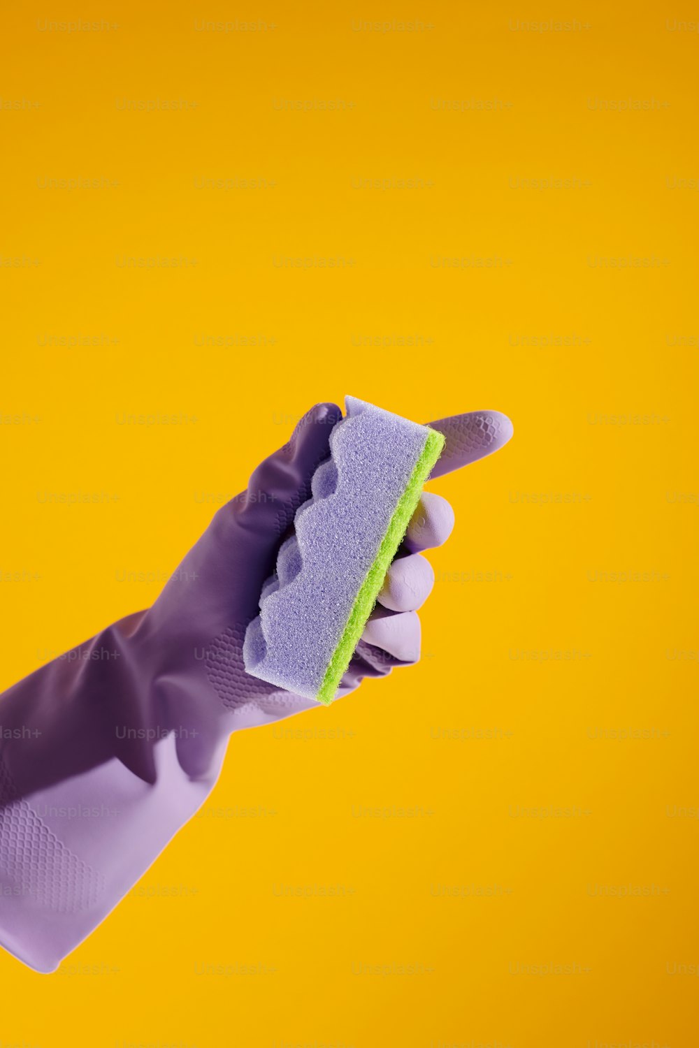 un guante púrpura sosteniendo una esponja sobre un fondo amarillo