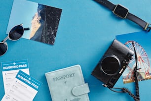 青い表面に並べられたパスポート、サングラス、カメラ、その他のアイテム