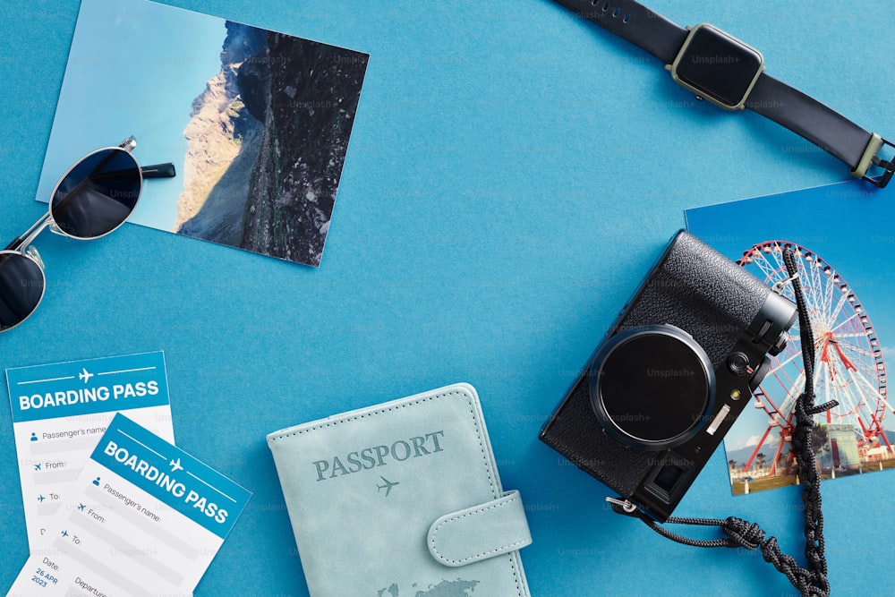 um passaporte, óculos escuros, câmera fotográfica e outros itens dispostos em uma superfície azul